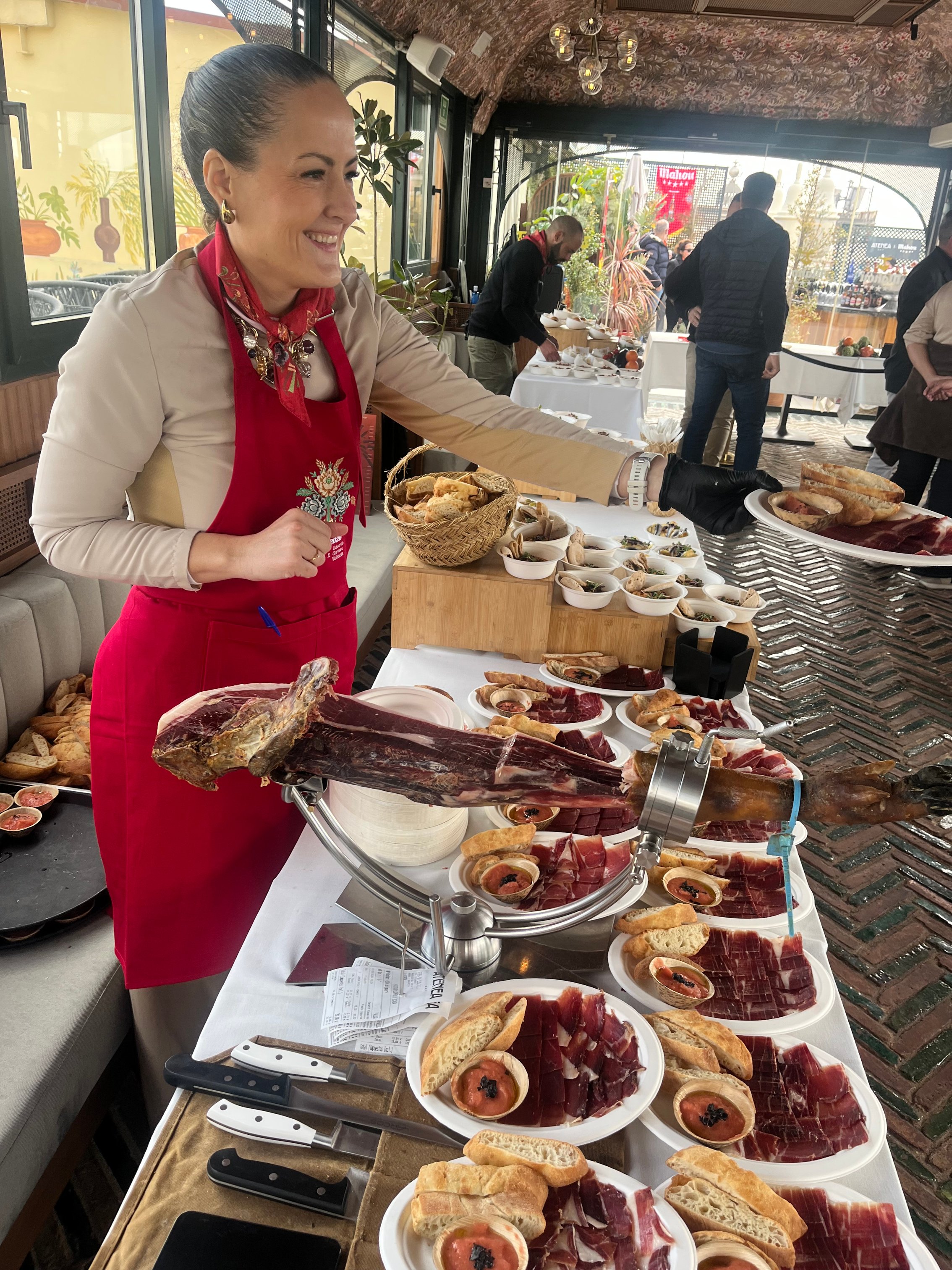 Mireia Sanchis cortando jamón ibérico junto a una mesa de aperitivos en un evento