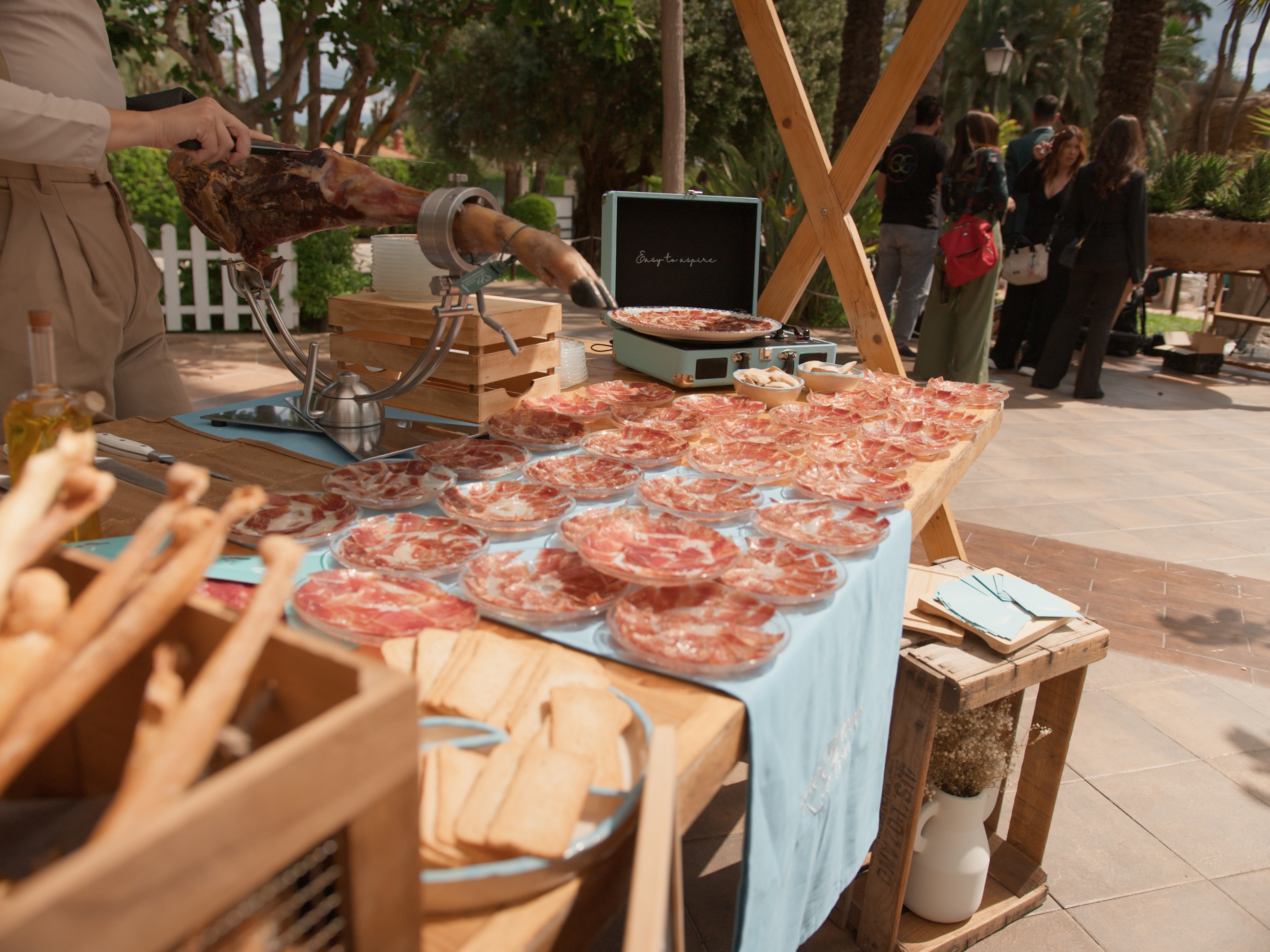 Mesa de evento con platos de jamón ibérico cortado a cuchillo y Mireia Sanchis cortando al fondo
