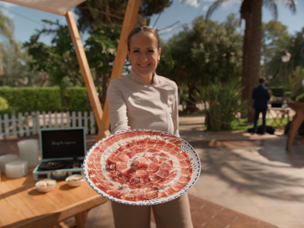 Mireia Sanchis sosteniendo un plato de jamón ibérico cortado a cuchillo en un evento al aire libre